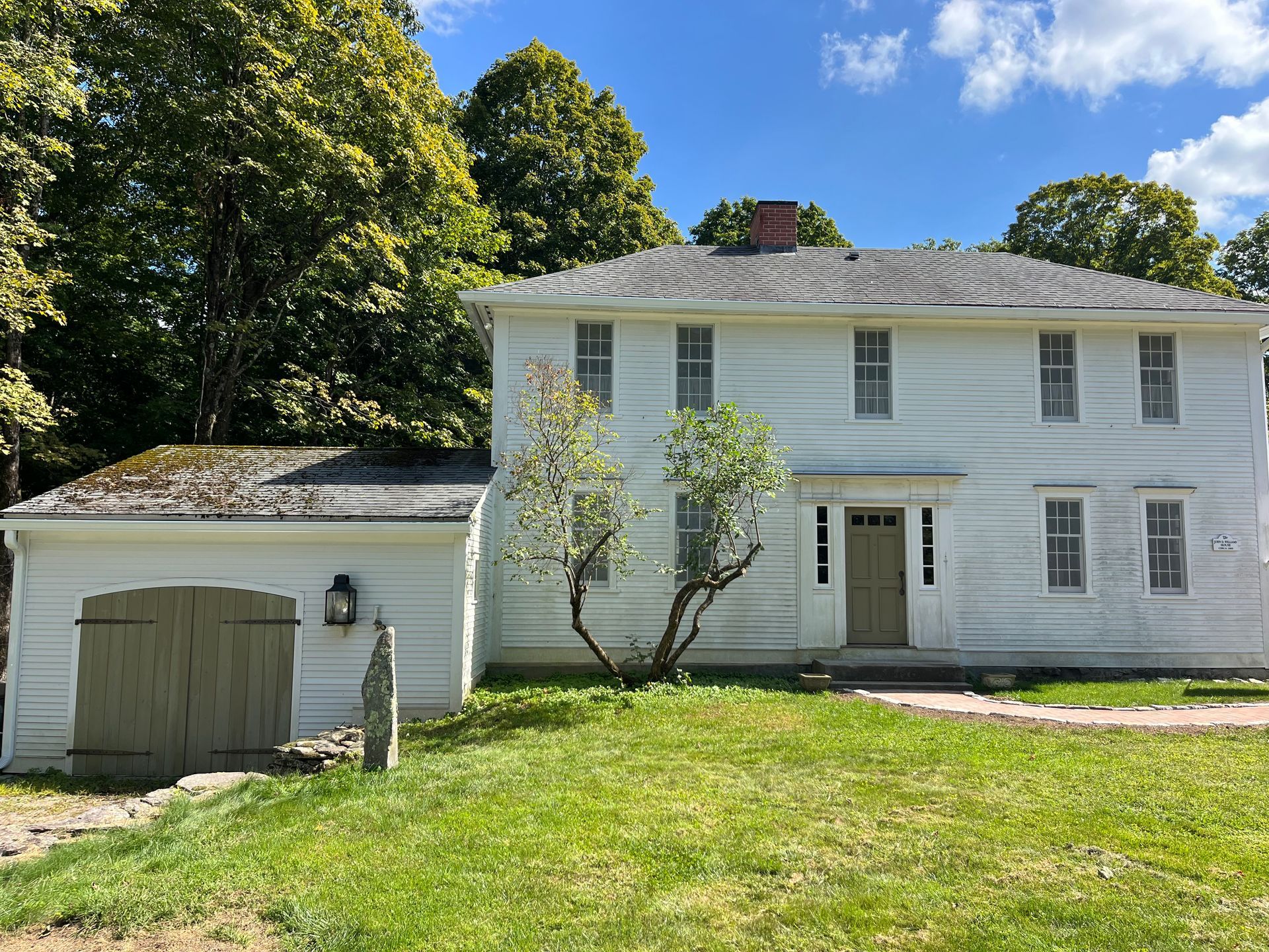 White two-story house with attached garage, front lawn, and trees in bright daylight
