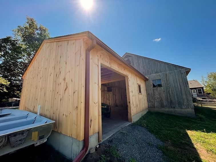 Wooden garage with open doorway beside a weathered shed on a sunny day