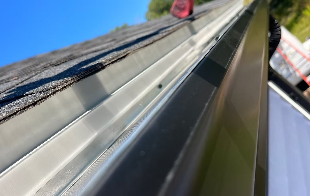 Close-up of a reflective metal gutter or roof edge against blue sky and building facade