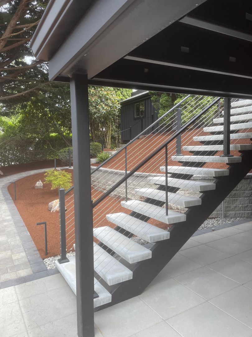 Modern outdoor staircase with dark railings and white steps beside a brick wall and landscaped area