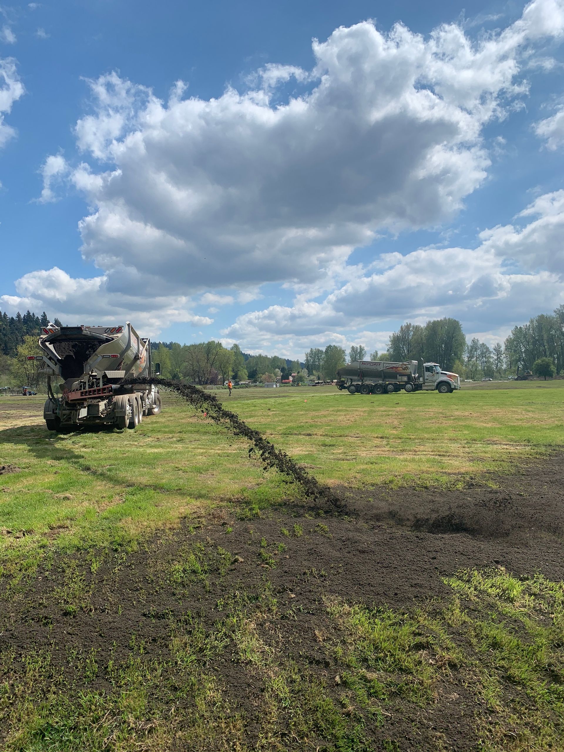 Agricultural machinery harvesting a muddy field under a cloudy blue sky