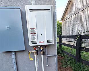 A white water heater is attached to a wall next to a fence.