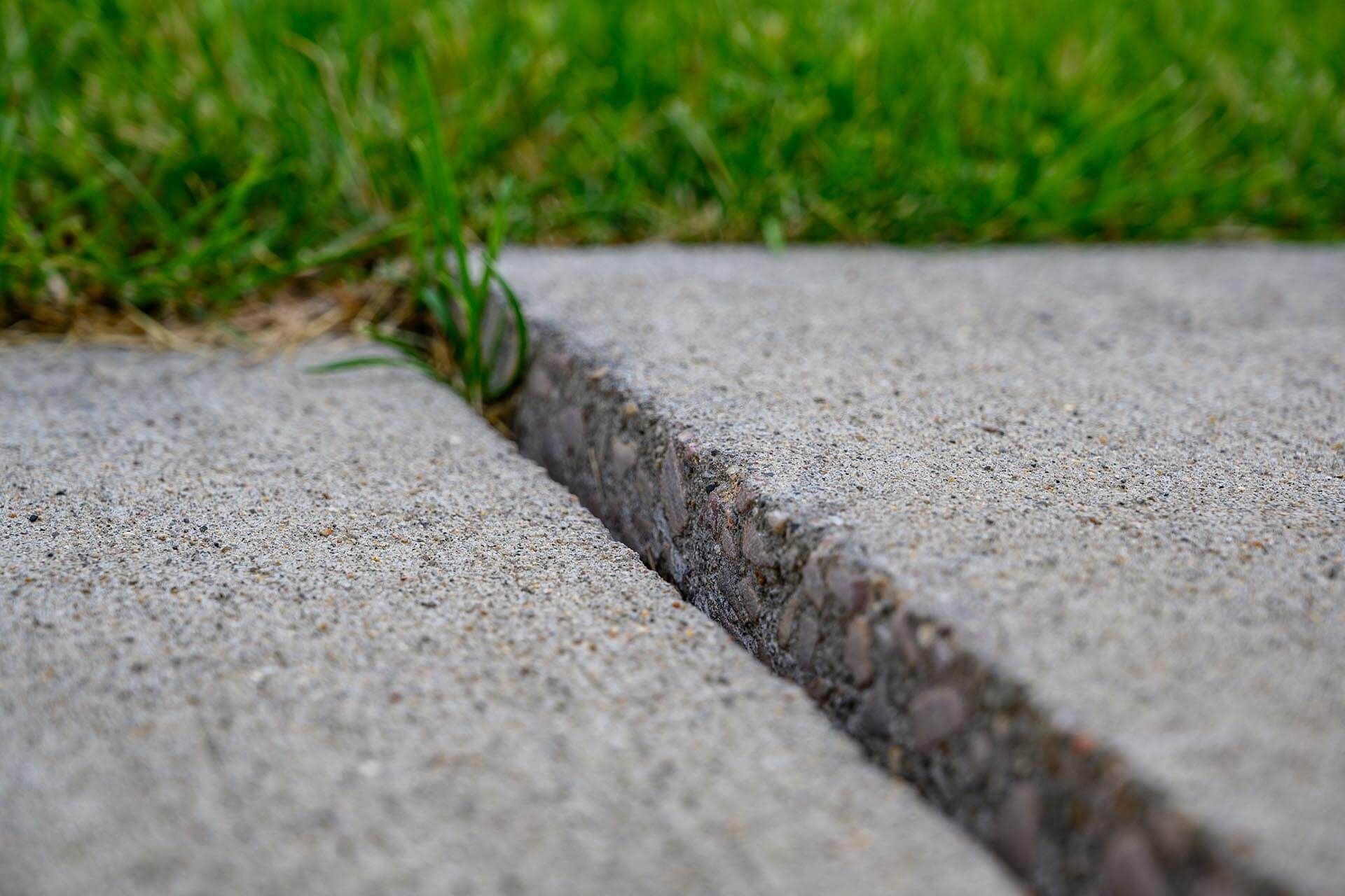 Cracked concrete walkway with grass growing through the gap
