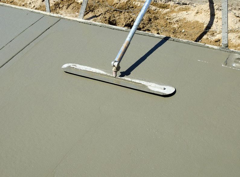 A concrete worker smoothing wet cement with a long-handled screed tool.