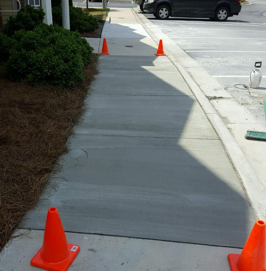 Concrete driveway with basketball hoop, garage, and small house on a bright day.