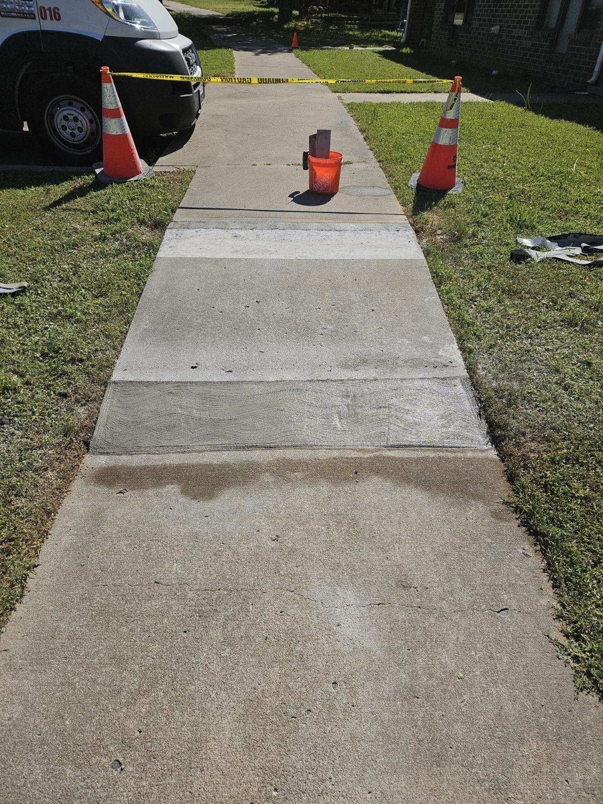 Sidewalk blocked with cones and caution tape; emergency vehicle visible. A bucket and a section of wet concrete.