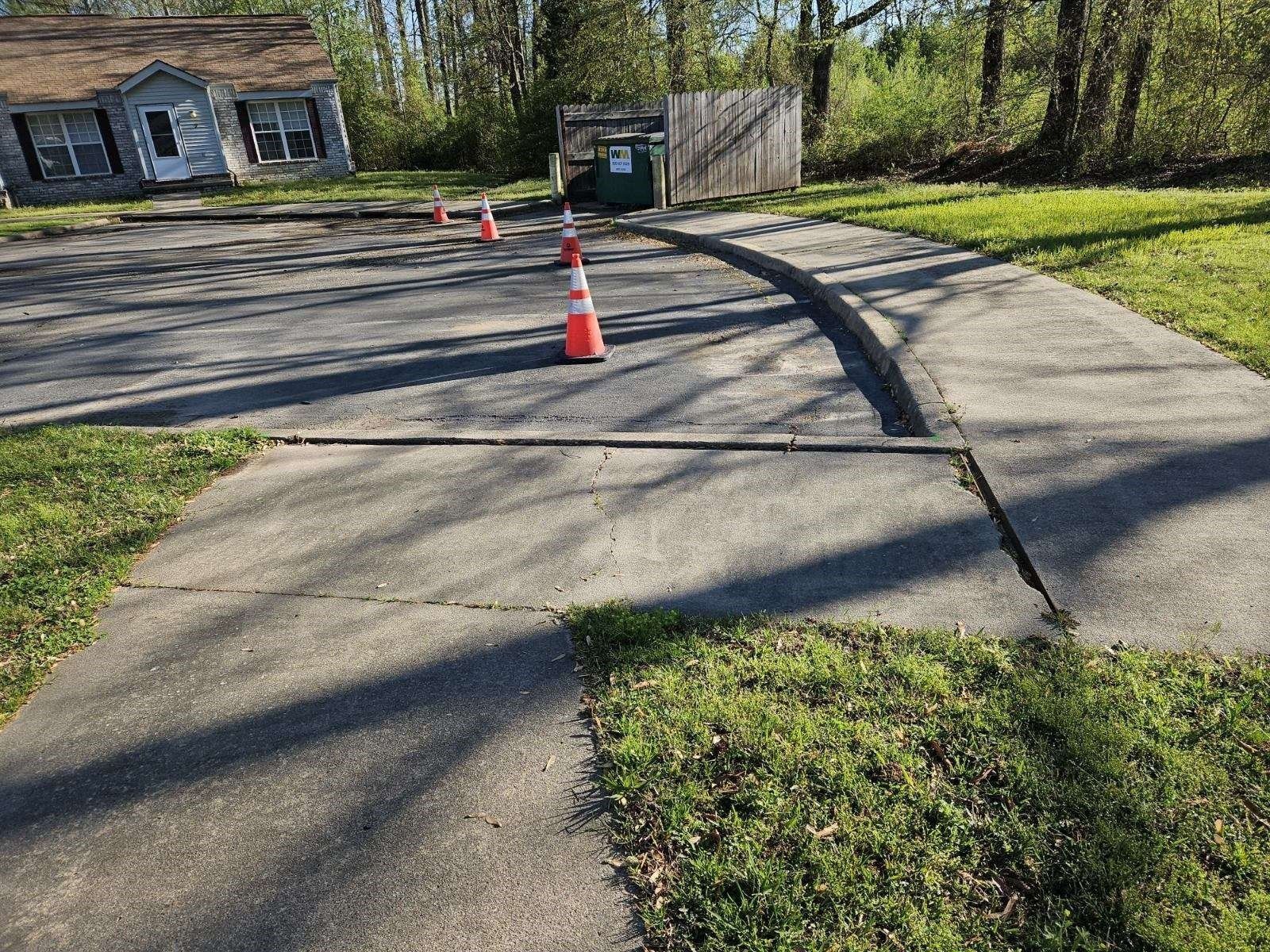 Concrete driveway with orange cones, grass, and a house in the background.