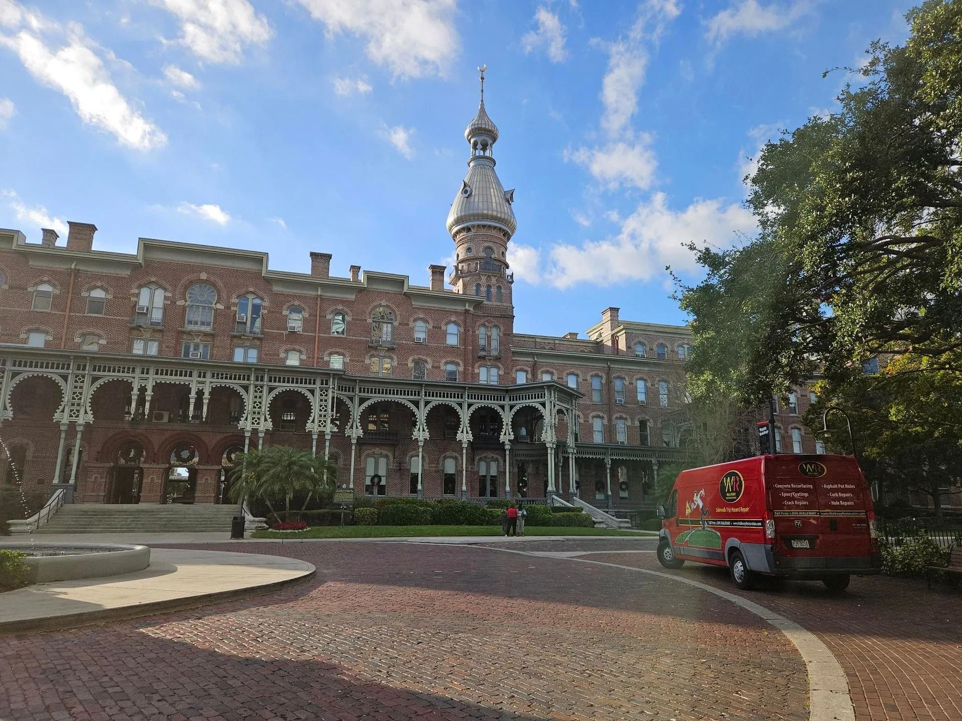 Brick building with tower, red truck on brick road, and blue sky.