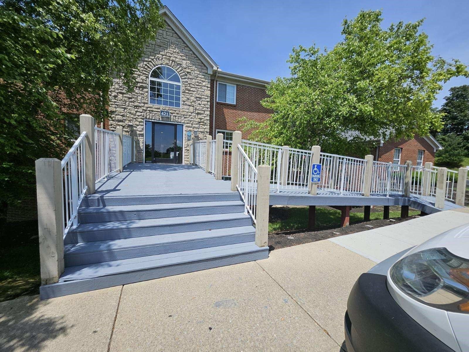 Exterior view of building with a ramp and steps leading to the entrance; blue steps and deck, light gray railings.