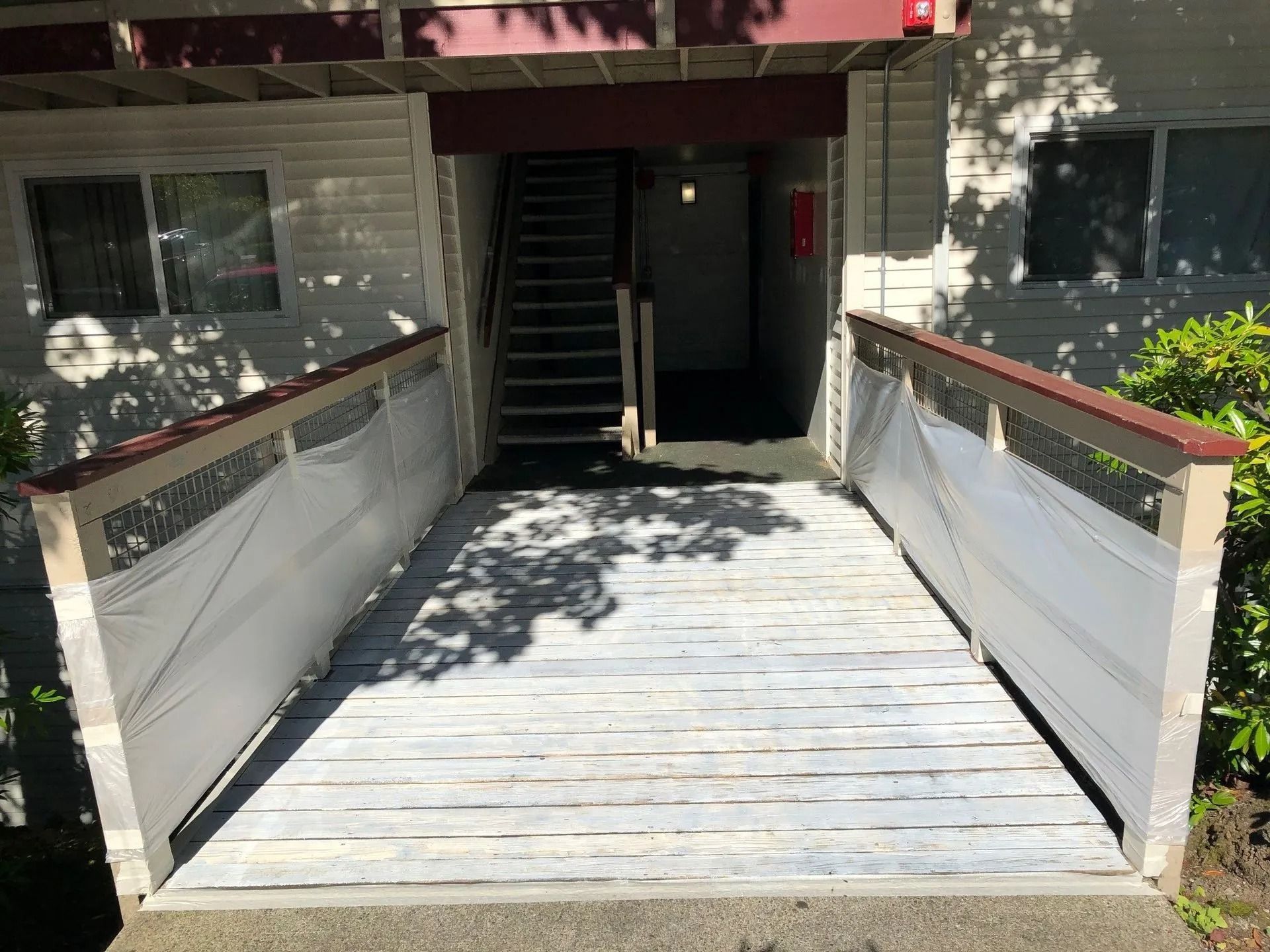 Wooden ramp leading to building entrance, with stairs visible. White railing and weathered wood.