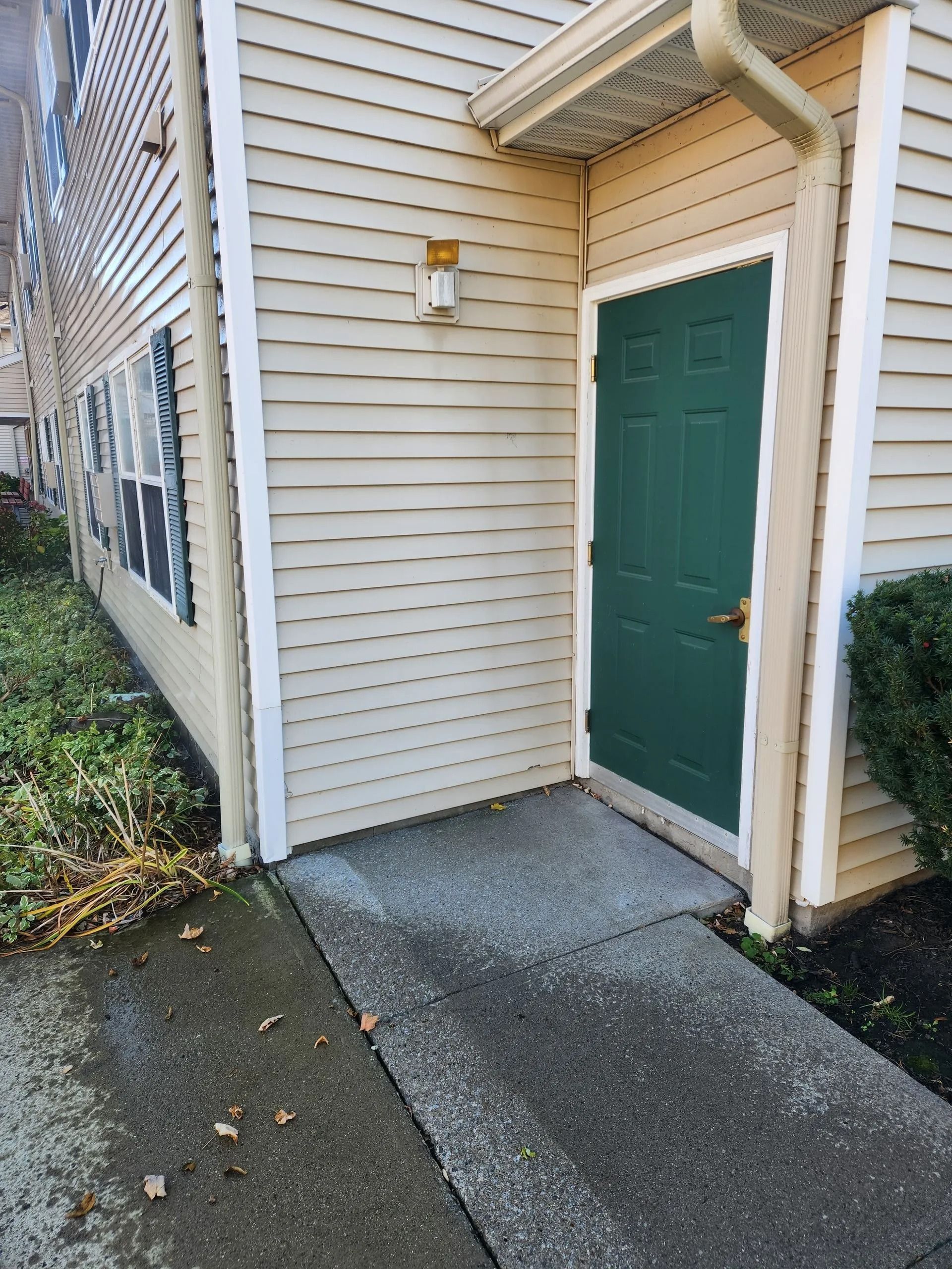 A beige building with a green door and concrete walkway.