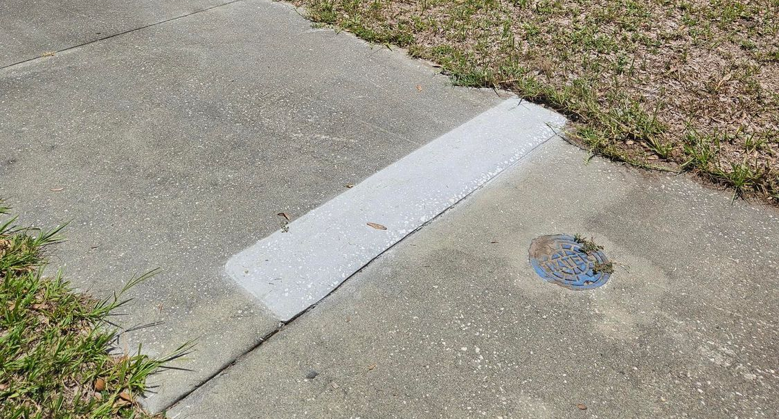 Construction worker smoothing wet concrete on a road repair site with a leveling tool, orange safety cones present.