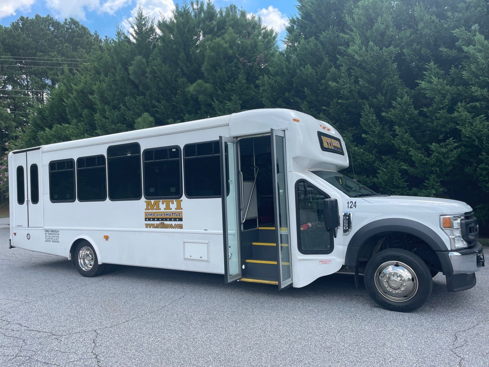 White shuttle bus parked on gravel, with trees in the background.