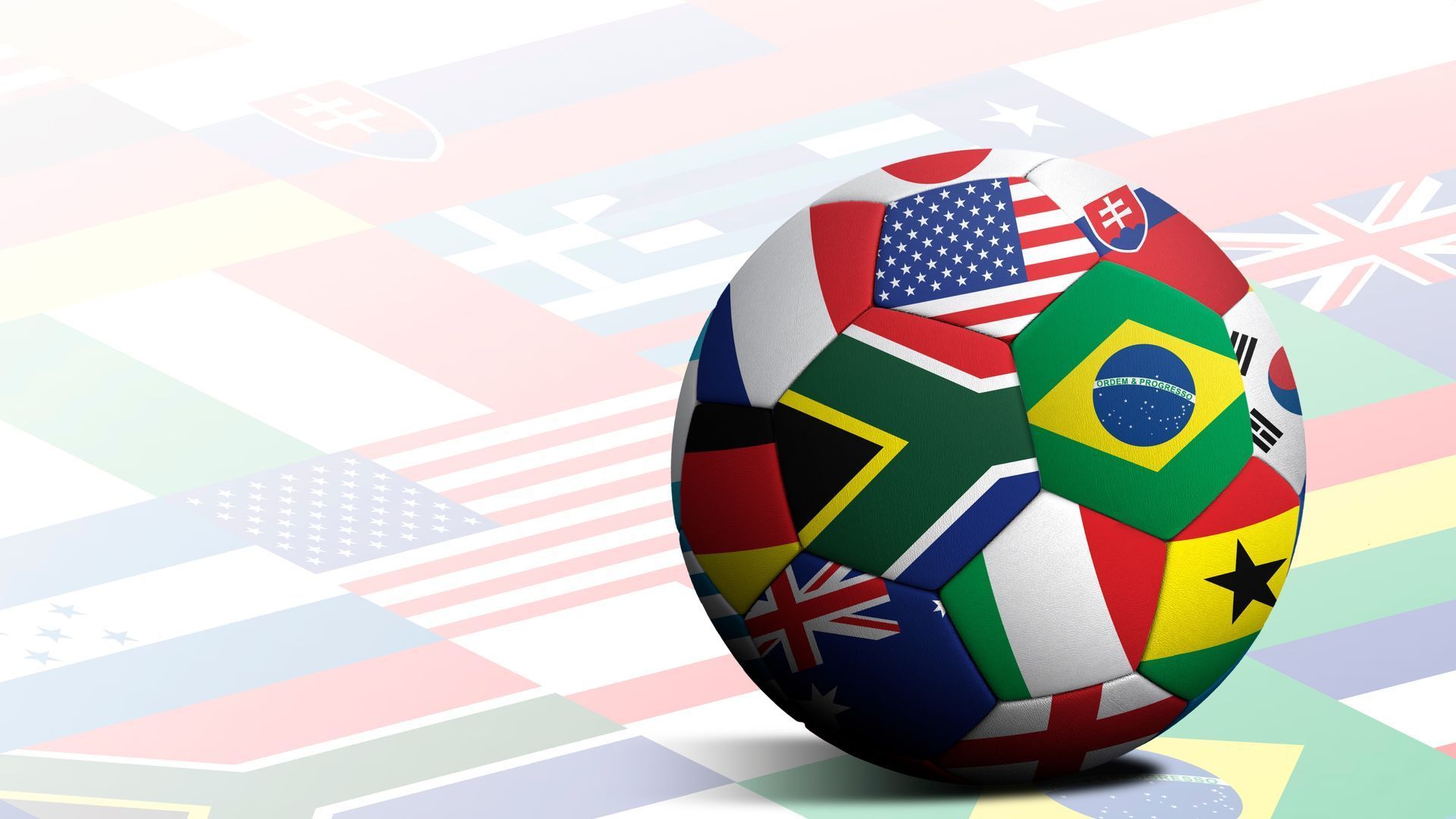 Soccer ball decorated with flags of many nations, with a blurred flag background.