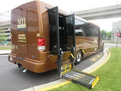 Brown shuttle bus with open doors and deployed wheelchair lift at a curb.