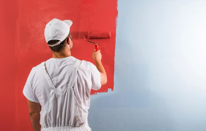 Person painting a wall red with a roller, next to an unpainted white section