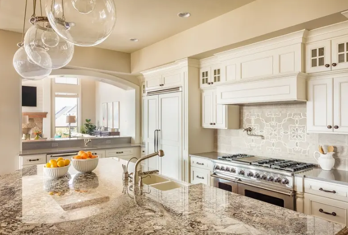 Bright modern kitchen with white cabinets, granite island, stainless stove, and hanging glass pendant lights