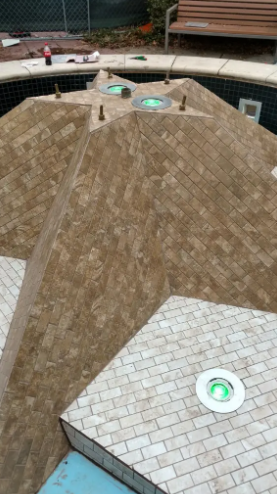 A tiled, star-shaped water fountain feature with embedded lights in a swimming pool area.
