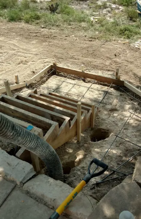 Wooden formwork for a set of concrete steps under construction, with a shovel in the foreground and wire mesh on dirt.