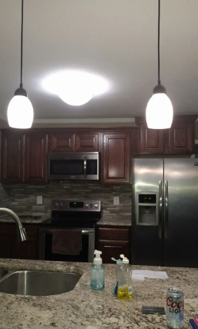 A kitchen featuring dark wood cabinets, stainless steel appliances, granite countertops, and two pendant lights overhead.