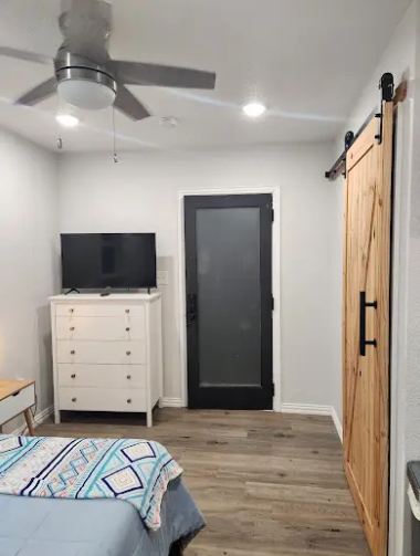 A bedroom featuring light gray walls, wood floors, a white dresser with a TV, a black-framed glass door, and a barn door.