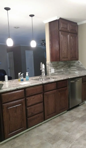 A kitchen featuring dark wood cabinets, a speckled granite countertop, a stainless steel dishwasher, and two pendants.