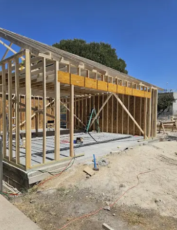 A wooden frame structure under construction on a concrete foundation under a clear blue sky.