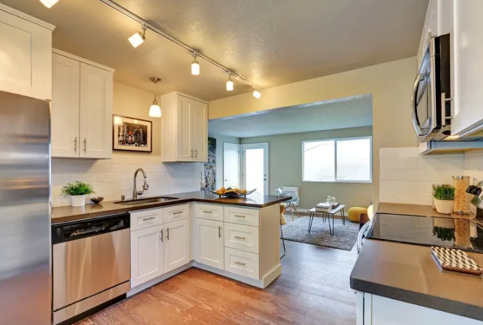 Bright modern kitchen with white cabinets, stainless appliances, and a view into a sunlit living area