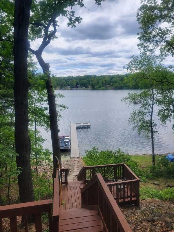 Wooden deck stairs leading to a dock on a calm lake, framed by trees under cloudy skies.