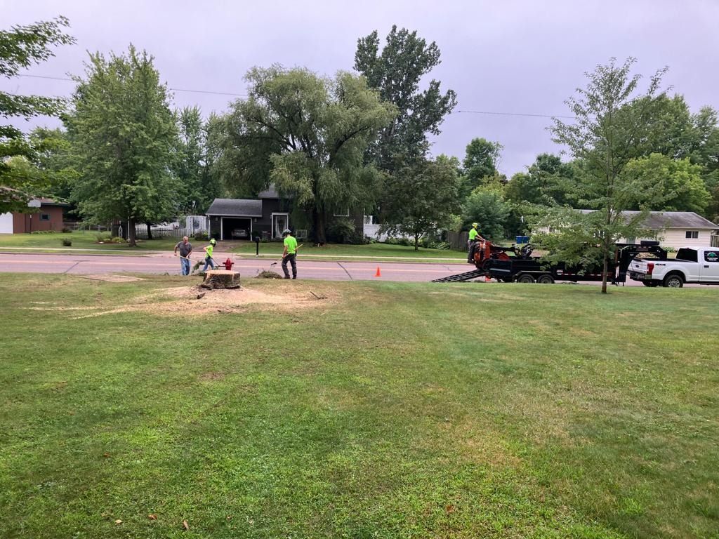 Workers repairing a road in a grassy neighborhood park with equipment and a truck nearby