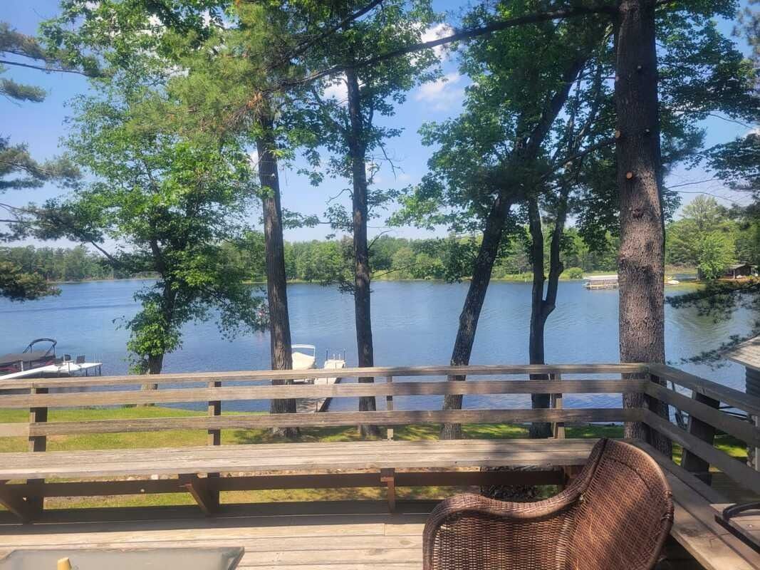 Lake view from a wooden deck with trees, railing, and a wicker chair.