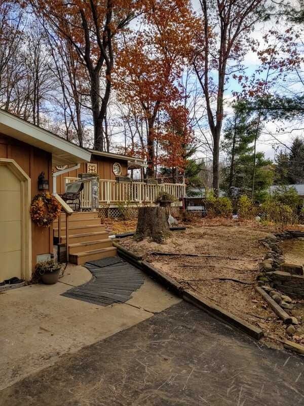Backyard with beige house, deck, and leafless trees beside a dirt-covered yard and driveway.