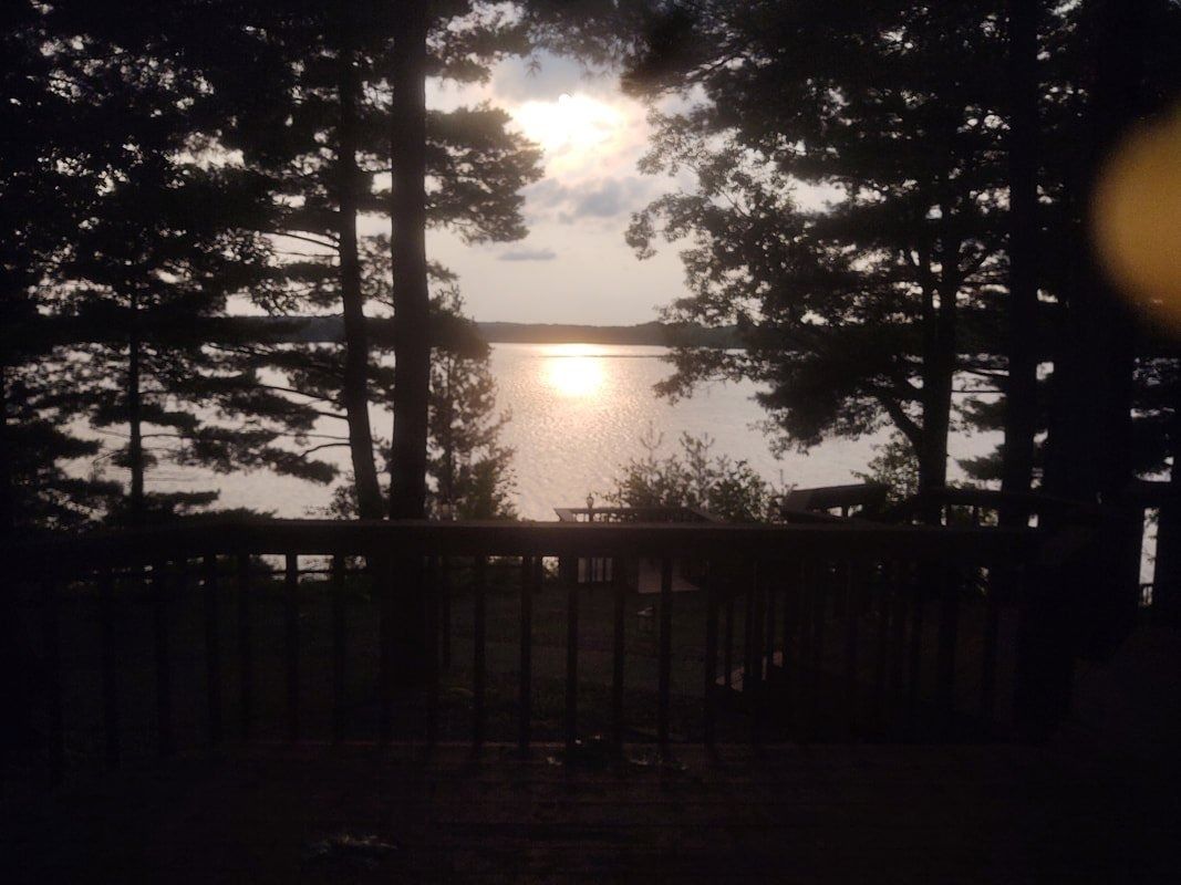 Sunset over a lake framed by dark trees and a wooden deck railing
