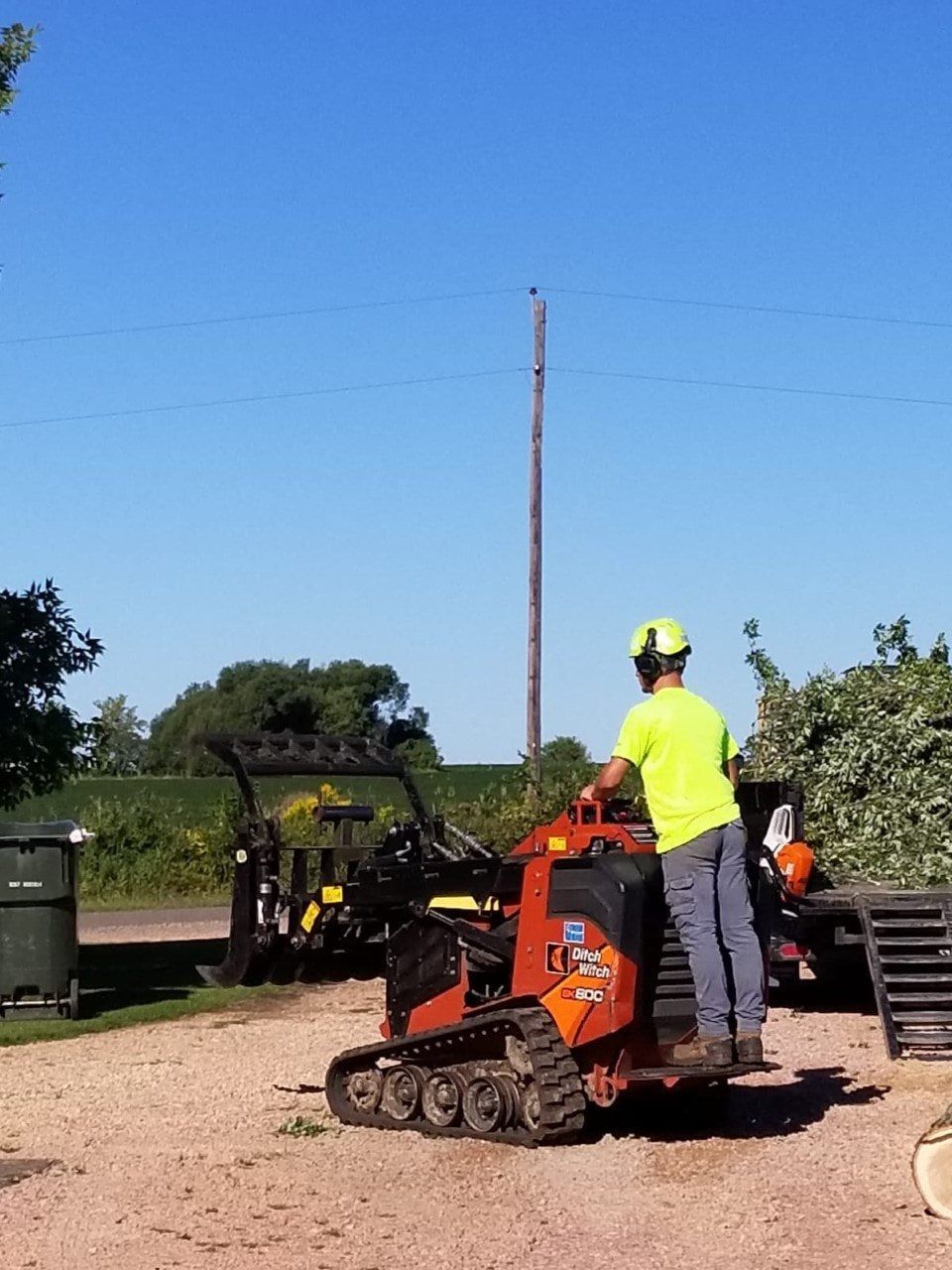 Worker in neon shirt standing on an orange tracked machine in a gravel field under a blue sky