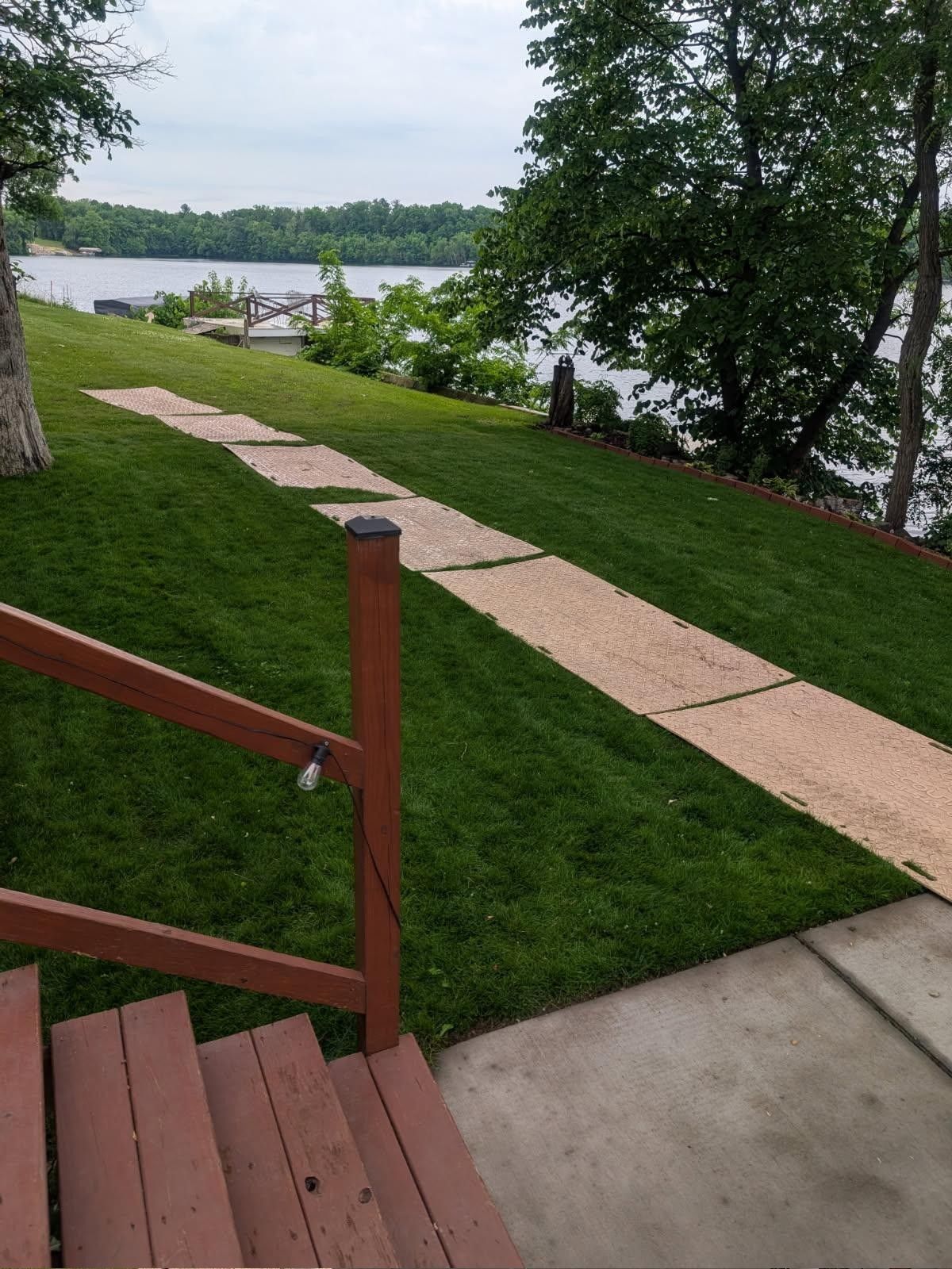 Stairway to a lakeside lawn with a paved path, trees, and water in the background