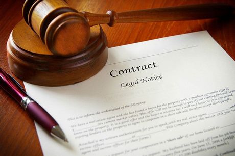 Gavel on a wooden block next to a contract and a pen, indicating legal proceedings.