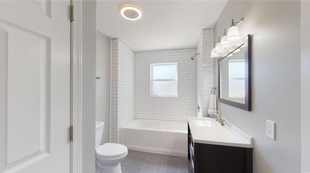 A bathroom with a toilet , sink , tub and mirror.