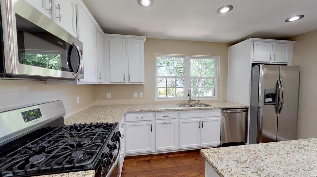 A kitchen with white cabinets , stainless steel appliances and granite counter tops.