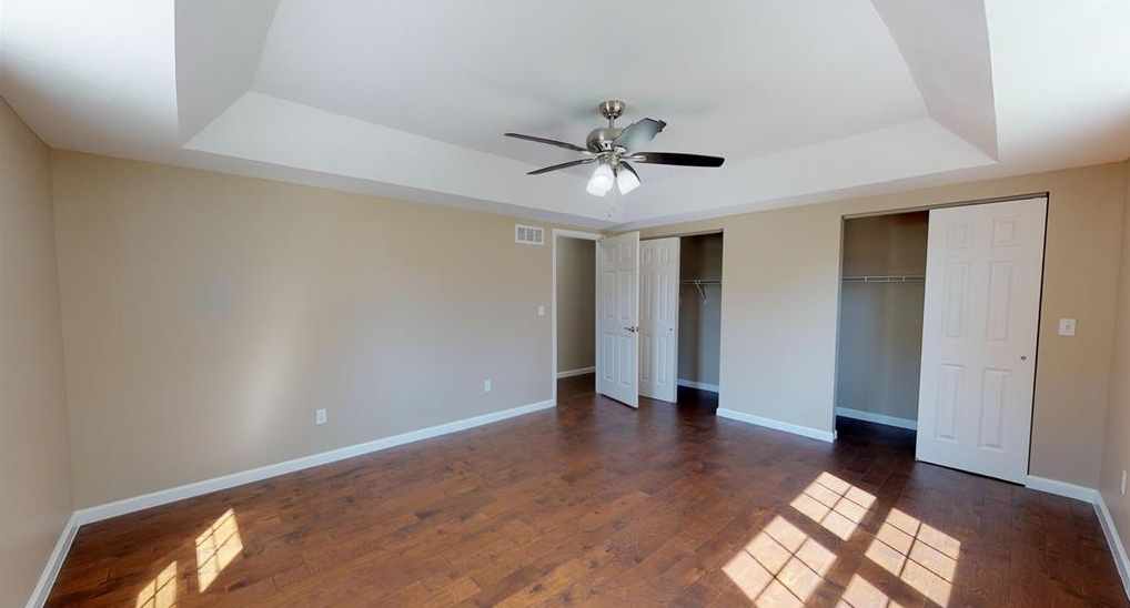 An empty bedroom with hardwood floors and a ceiling fan.