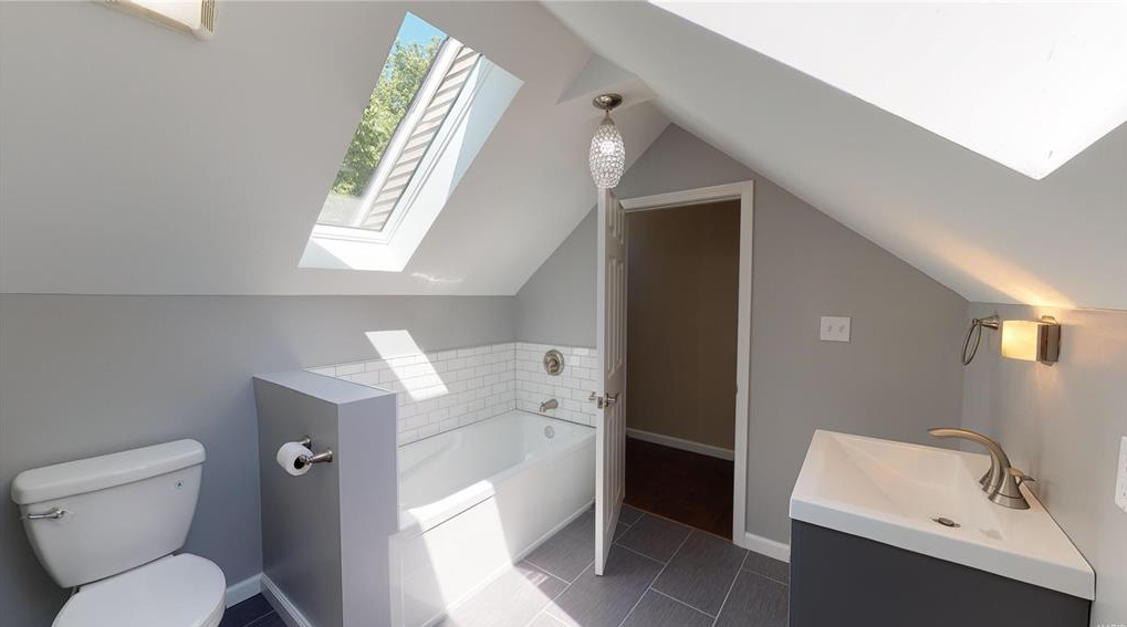A bathroom with a toilet , sink , bathtub and skylight.