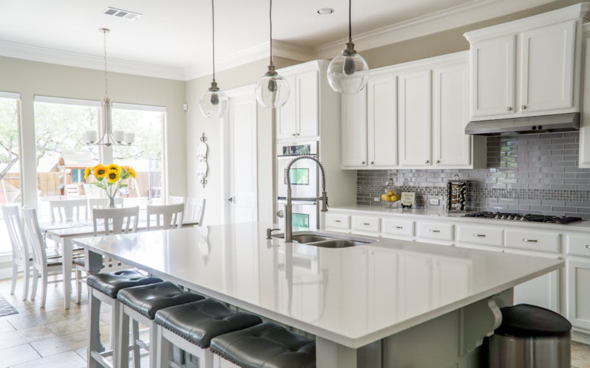 A kitchen with white cabinets and a large island with stools.