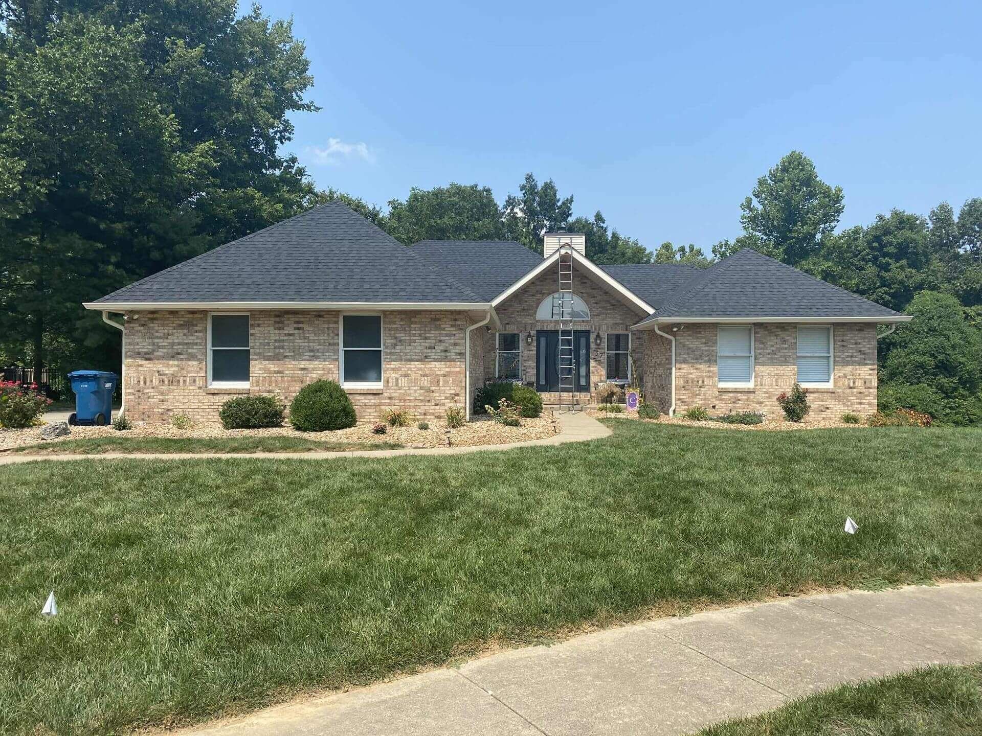 Tan brick house with a dark roof and manicured lawn. Clear blue sky.