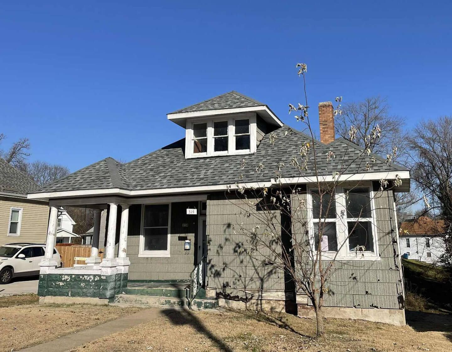 Gray house with a porch, dormer, and chimney against a clear blue sky.