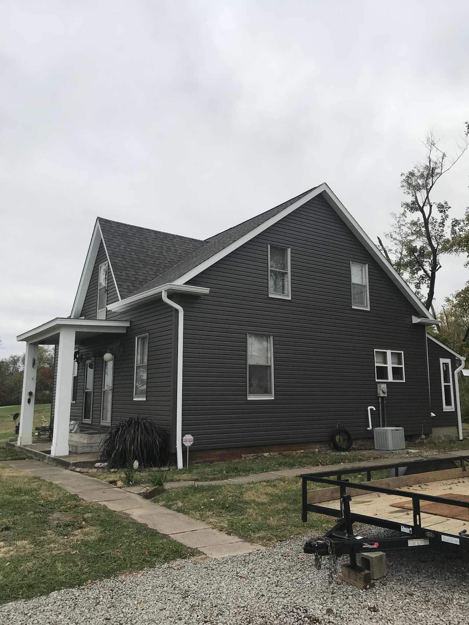 Two-story house with dark gray siding, white trim, and a porch under a cloudy sky.