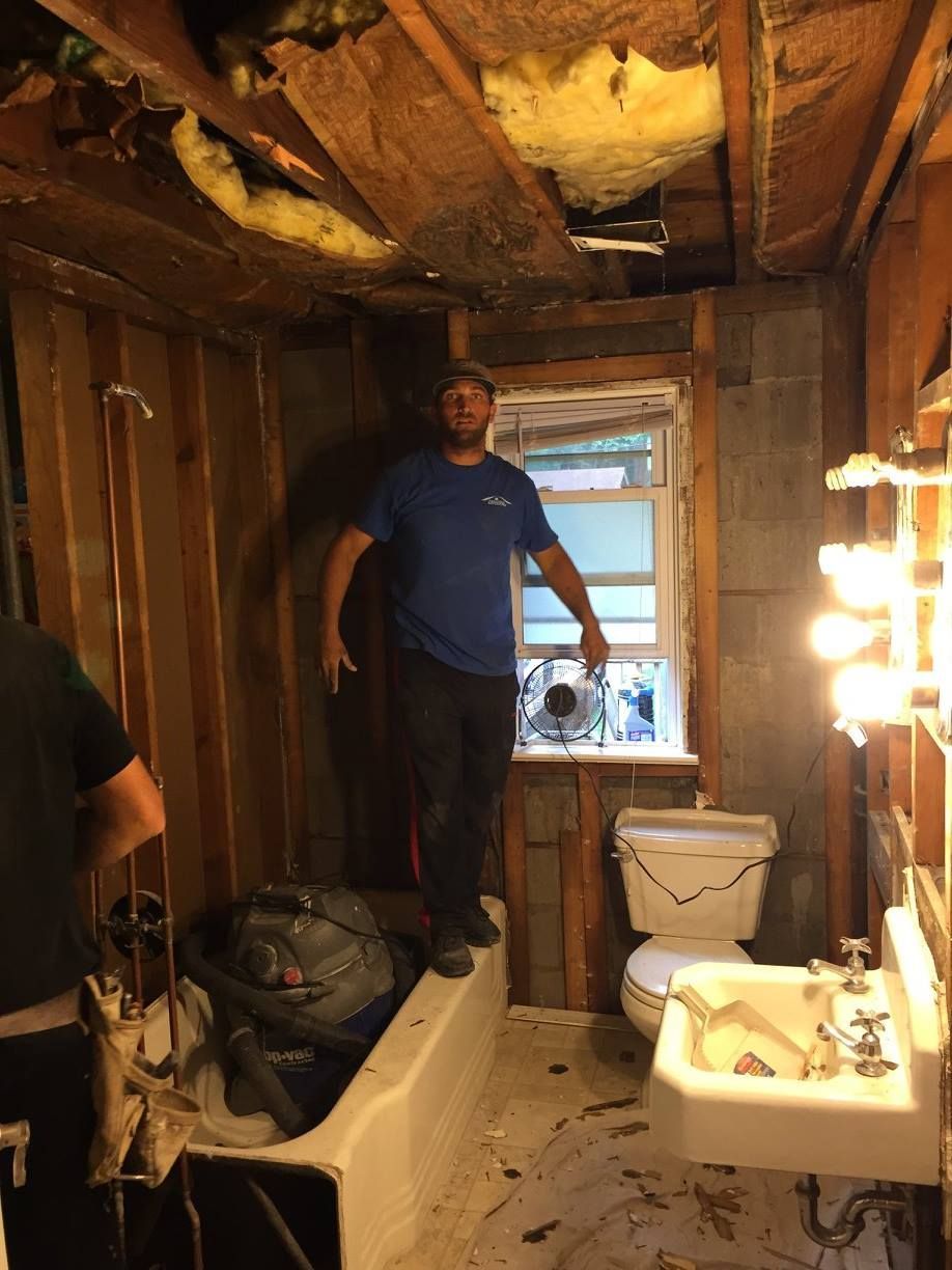 A man is standing on a bathtub in a bathroom under construction.