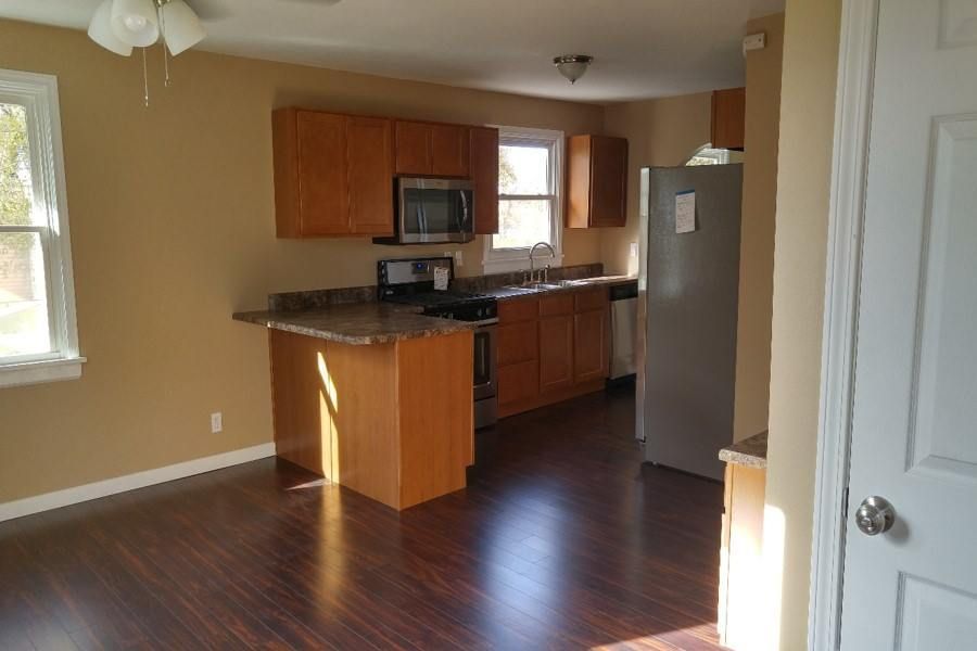 An empty kitchen with wooden cabinets , a refrigerator , and a microwave.