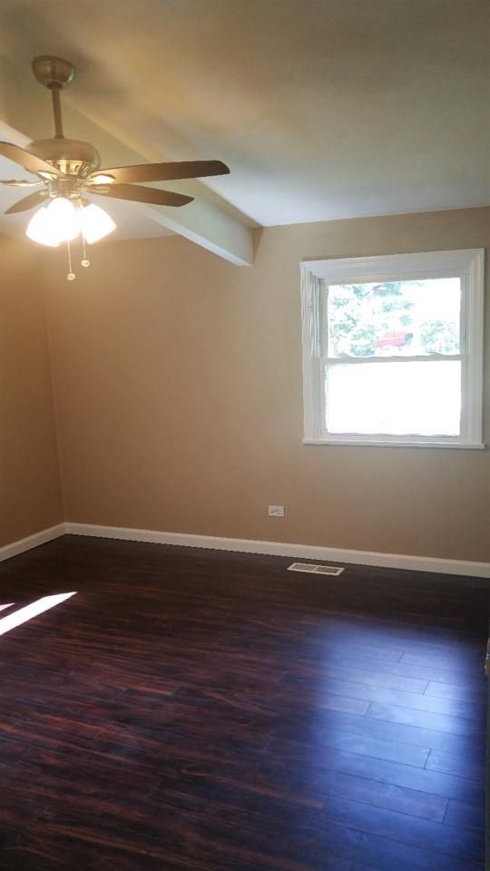 An empty living room with a ceiling fan and a window.