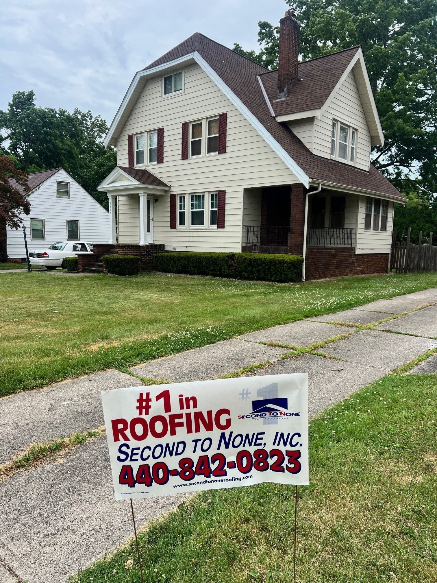 A sign for a roofing company is in front of a house.