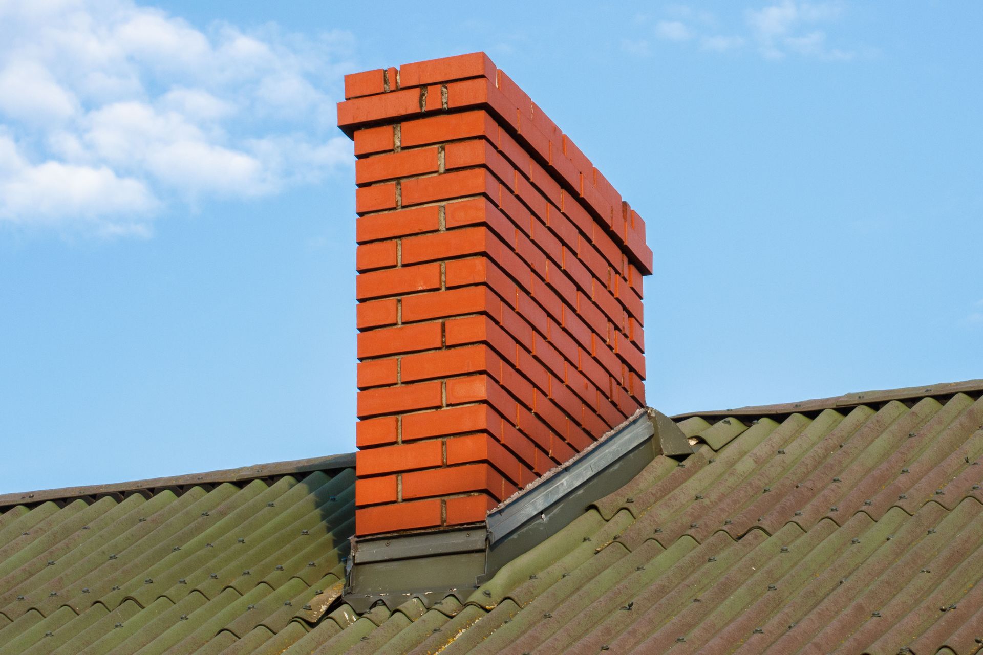 Brick chimney on a green-tiled roof against a blue sky.