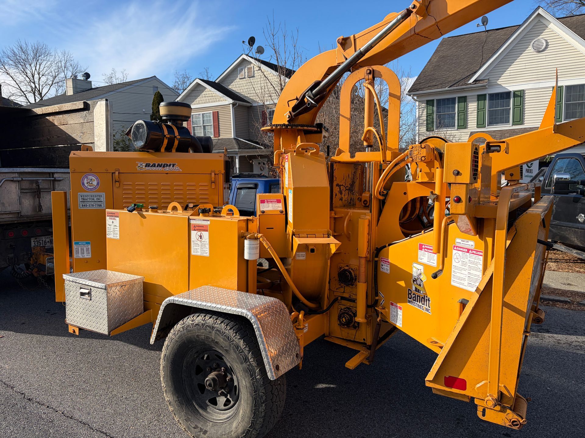 Yellow wood chipper on a trailer parked on a street with houses in the background.